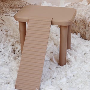 May include: A small, tan-colored pet habitat accessory. The structure includes a square platform supported by four cylindrical legs, with a textured ramp extending from the platform. The ramp has horizontal ridges. The accessory is designed for small pets.