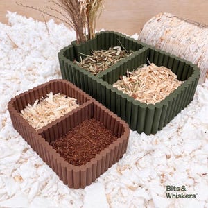 Puede incluir: Dos recipientes rectangulares de múltiples compartimentos con una textura exterior acanalada. Un recipiente es de color verde oliva oscuro y contiene hierba seca y virutas de madera. El otro es marrón y contiene virutas y tierra oscura.