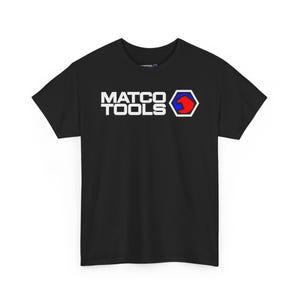 Può includere: T-shirt nera con la scritta bianca "MATCO TOOLS" e un logo rosso, blu e bianco. Il logo è un esagono stilizzato con un design blu e rosso. La maglietta è a girocollo e maniche corte.