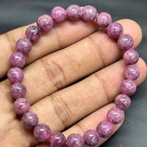 May include: A white ceramic mug with a black handle and the text "But First, Coffee" in a bold, black font. The mug is set against a blurred background, suggesting a cozy setting.