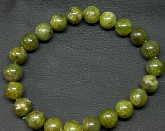May include: A green beaded bracelet composed of round, polished beads. The beads have a mottled appearance with variations in the green color. The bracelet is strung on a green elastic cord. The beads are approximately 0.75 inches in diameter.