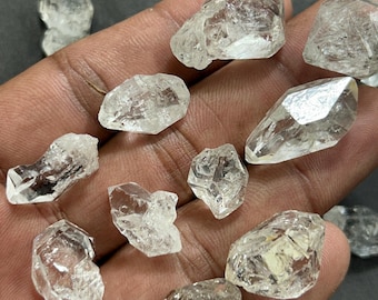 Könnte beinhalten: Eine Sammlung klarer, grob geschnittener Quarzkristalle. Die Kristalle variieren in Größe und Form, mit sichtbaren Facetten und inneren Strukturen. Sie werden vor einem dunklen Hintergrund präsentiert, was ihre Klarheit und natürliche Schönheit hervorhebt.