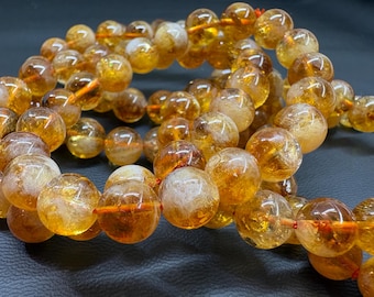 May include: A strand of round, translucent, golden-yellow beads with internal cloudy white inclusions. The beads are strung together on a thin, bright orange cord, creating a continuous loop of polished, spherical stones with varying colour depth.