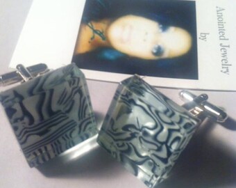 May include: A pair of cufflinks with a black and white abstract design. The cufflinks are made of glass and have a silver metal backing. The text "Anointed Jewelry by" is visible in the background.
