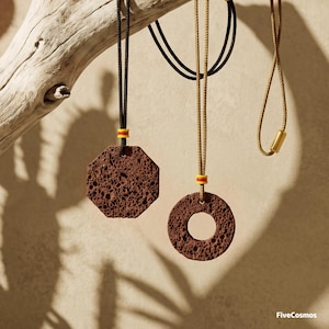 Puede incluir: Dos collares con colgantes de roca volcánica de color marrón oscuro y textura porosa. Un colgante es octogonal y el otro circular. Ambos cuelgan de cordones finos con pequeñas cuentas amarillas y rojas. El texto FiveCosmos es visible.