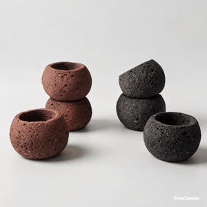 May include: A collection of five small, spherical, porous planters with a rough, volcanic rock-like texture. Two planters are reddish-brown, and three are dark charcoal gray. The text FiveCosmos is printed in the bottom right corner.