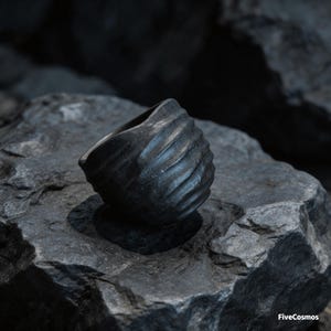May include: A dark charcoal gray ring with a textured, rippled surface featuring horizontal grooves. The ring has a rounded, organic shape and a matte finish. The text FiveCosmos is visible in the bottom right corner of the image.