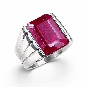 May include: A silver ring featuring a large, rectangular, deep red gemstone. The ring has a wide band with a simple, modern design. The text "Lunoviamakes" is engraved on the band.