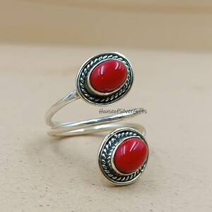 Pode incluir: Um anel prateado com duas pedras ovais vermelhas brilhantes. Cada pedra está engastada numa moldura decorativa e texturizada. A banda do anel envolve o dedo. O texto "HouseofSilverGifts" é visível.