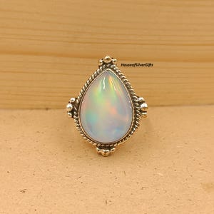 May include: A pear-shaped opal ring with a silver band. The opal has a milky white base with iridescent flashes of color. The ring has a detailed, textured silver setting with decorative elements around the stone.