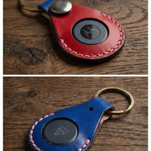 May include: Leather keychains in red and blue with a metal ring. The red keychain has a black circle with a Motorola logo. The blue keychain has a black circle with a triangle logo. Both keychains have pink stitching.