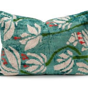 May include: A rectangular throw pillow featuring a teal velvet base with a repeating floral pattern in cream, green, and orange. The fabric has a textured, plush appearance with a soft sheen, showcasing stylized flower motifs across the surface.