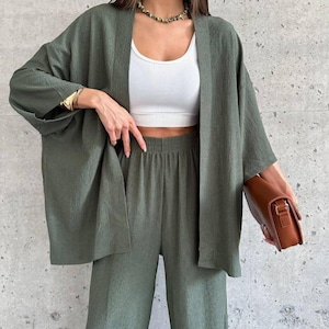 May include: A two-piece set in olive green featuring a loose-fitting, open-front kimono-style jacket with wide sleeves and matching high-waisted, wide-leg trousers. The fabric has a subtle, crinkled texture throughout the entire garment set.