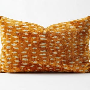 May include: A rectangular throw pillow featuring a vibrant mustard yellow and orange velvet fabric with a repeating pattern of small, light cream-colored horizontal dashes that resemble a spotted animal print across the entire surface.