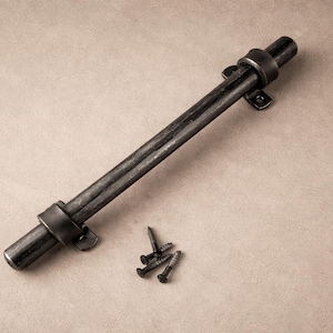 May include: A dark gray metal gate latch with a cylindrical handle and mounting hardware. The latch is lying on a neutral-toned surface, with a small pile of screws nearby. The hardware appears to be made of wrought iron.