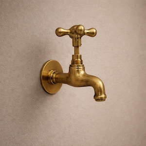 May include: A brass tap with a cross-shaped handle and a curved spout. The tap is mounted on a round base and is made of a shiny, golden metal. The fixture is designed for wall mounting.