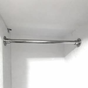 Könnte beinhalten: Eine verchromte Kleiderstange, die zwischen zwei weißen Wänden installiert ist. Die Stange ist zylindrisch und hat kreisförmige Montageplatten an jedem Ende. Zum Aufhängen von Kleidung.