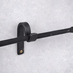 May include: A black metal towel bar with a rounded end and a curved bracket for wall mounting. The bar is approximately 18 inches long and has a matte finish. The bracket is secured with a single gold screw.