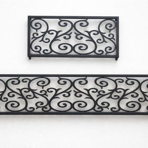 Puede incluir: Dos paneles decorativos de hierro forjado negro con un diseño floral en espiral. Un panel es rectangular y el otro es un rectángulo más pequeño. Los paneles están montados en una pared blanca.
