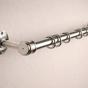 May include: A polished chrome curtain rod with rings, mounted on a wall. The rod has a cylindrical design with a series of circular rings for hanging curtains. The mounting hardware is also chrome, creating a cohesive look.