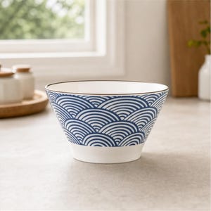 May include: A white ceramic bowl featuring a repeating blue wave pattern around the exterior. The bowl has a wide, open top with a thin brown rim and a solid white base. The interior of the bowl is plain white, and the design consists of concentric semicircles.