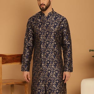 May include: A navy blue kurta with a gold floral design. The long-sleeved tunic has a mandarin collar and a tailored fit. The outfit is completed with beige trousers, creating a coordinated look. The fabric has a subtle sheen, enhancing the overall elegance of the outfit.