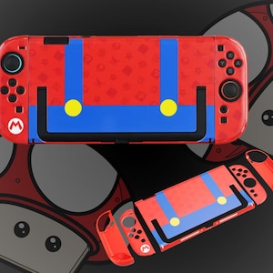 Könnte beinhalten: Rote und blaue Nintendo Switch-Hülle mit Mario-Design. Die Hülle hat einen roten Hintergrund mit blauen Hosenträgern, gelben Knöpfen und einer schwarzen Umrandung. Das Design wiederholt sich auf den abnehmbaren Controllern.