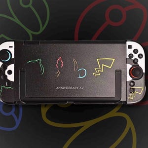 May include: Black game console with white accents and colorful character outlines. The console features the text "ANNIVERSARY XV". The background has colorful, abstract shapes.