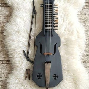 May include: A gray, stringed instrument with a bow and a wooden bridge, resting on a white, fluffy rug. The instrument has a unique shape with cross-shaped cutouts and a series of strings and keys.