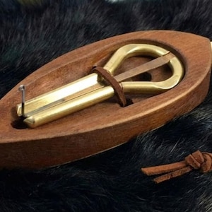 May include: A wooden jaw harp with a brass reed and a leather strap. The instrument is housed in a carved wooden case. The harp is a musical instrument, often used in folk music. The case is oval-shaped and has a smooth, polished finish.