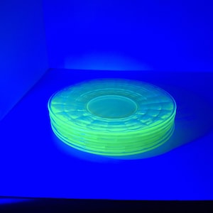 Op de afbeelding: Een stapel gloeiende, lichtgroene glazen borden. De borden zijn rond met een textuurontwerp en zijn gestapeld op een blauw oppervlak. De verlichting geeft de borden een heldere, bijna neonachtige uitstraling.