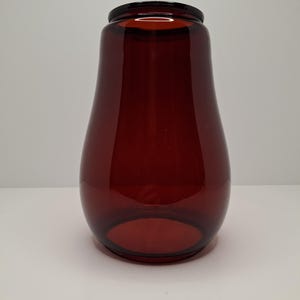 May include: A dark amber glass jar with a black lid. The jar has a rounded base and narrows towards the neck. The glass is transparent, allowing light to pass through. The jar is likely used for storage or decorative purposes.