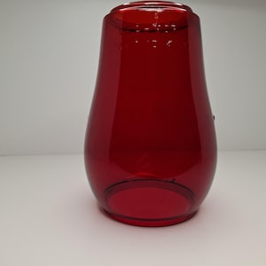 May include: A vibrant, ruby-red glass vase with a rounded base and a flared top. The vase has a smooth, glossy finish and a slightly tapered shape. The glass appears to be transparent, allowing light to pass through. The vase is likely used for decorative purposes.