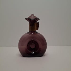 May include: A spherical, purple glass bottle with a decorative stopper. The bottle features a brass-coloured band around the neck. The stopper is a darker shade of purple and has a unique shape.