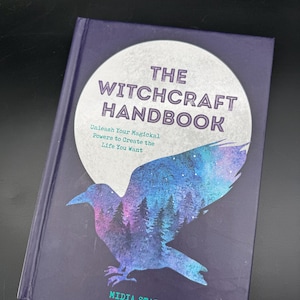 May include: A hardback book titled "THE WITCHCRAFT HANDBOOK" with a dark purple cover. The cover features a stylized raven silhouette with a forest and starry sky design. The text "Unleash Your Magickal Powers to Create the Life You Want" is also visible.