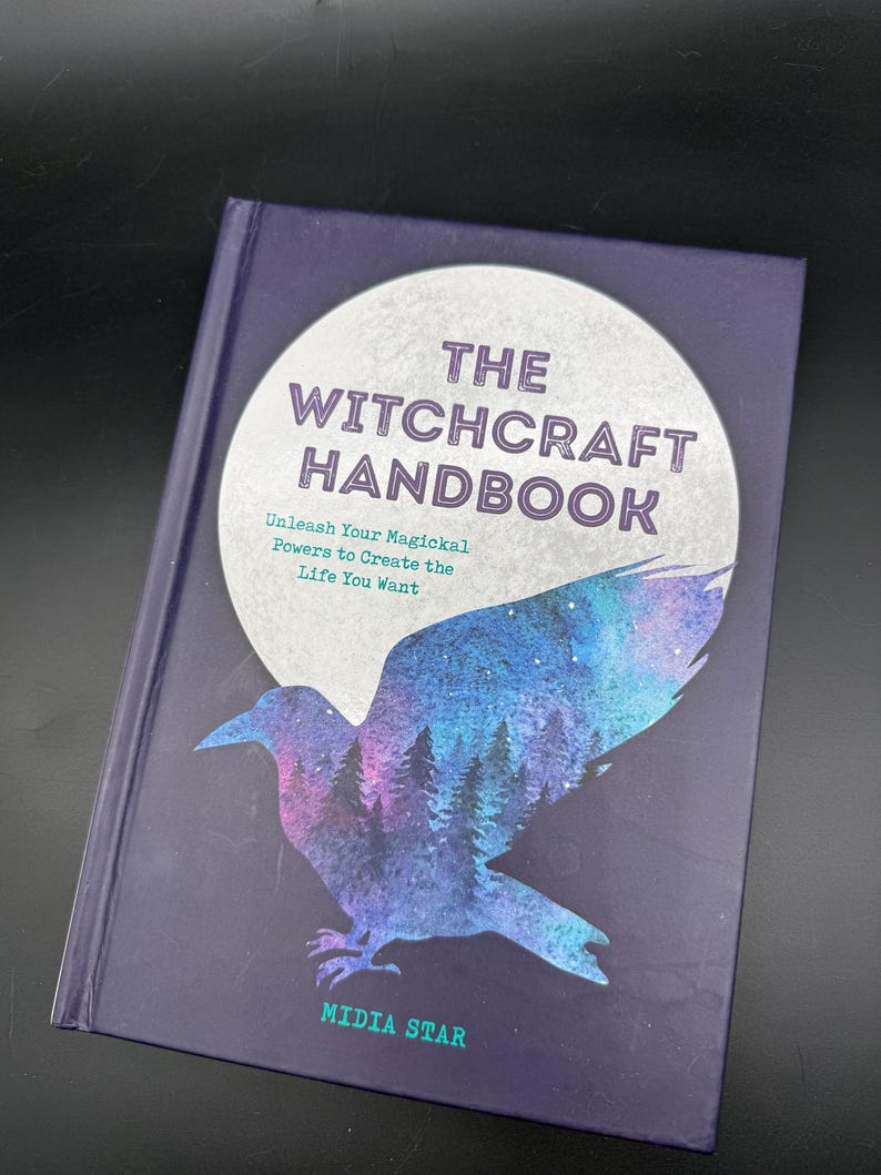 May include: A hardback book titled "THE WITCHCRAFT HANDBOOK" with a dark purple cover. The cover features a stylized raven silhouette with a forest and starry sky design. The text "Unleash Your Magickal Powers to Create the Life You Want" is also visible.