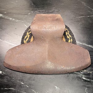 May include: A vintage brown metal iron with a rounded base and a handle. The iron is resting on a black and gold patterned pad. The text "HENRY" is visible on the handle.