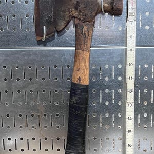 May include: A vintage hatchet with a wooden handle and a black grip. The metal head shows signs of wear and rust. The hatchet is approximately 11 inches long.