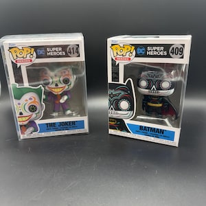 May include: Two Funko Pop! vinyl figures in their original boxes. The left box features The Joker, number 414, with a colorful sugar skull face design. The right box features Batman, number 409, with a black and white sugar skull face design.