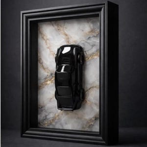 May include: A black toy car is mounted inside a black framed shadow box. The car is positioned vertically against a marble-patterned background. The frame has a simple, classic design, and the overall aesthetic is modern and minimalist.