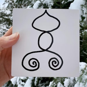 Puede incluir: Azulejo blanco cuadrado con un diseño abstracto negro. El diseño presenta una forma de lágrima en la parte superior, un círculo en el medio y dos espirales en la parte inferior. El azulejo se sostiene frente a un fondo de coníferas nevadas.