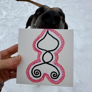 Puede incluir: Una baldosa cuadrada blanca con un diseño negro y rosa. El diseño presenta una forma negra central con un borde rosa punteado. Dos espirales negras están en la parte inferior. La cara de un perro es visible en el fondo, con un fondo nevado.