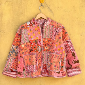 Può includere: Giacca trapuntata nei toni del rosa, pesca e arancione, con un design patchwork a motivi floreali e geometrici. Colletto alla coreana, chiusura con bottoni e bordi a righe su polsini e orlo.