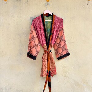 Könnte beinhalten: Ein leichter Morgenmantel im Kimono-Stil mit einem Patchwork aus verschiedenen Mustern und Farben, darunter Rosa-, Orange- und Grüntöne. Das Kleidungsstück hat lange Ärmel, einen schwarzen Saum entlang der Vorderseite und einen passenden Bindegürtel.