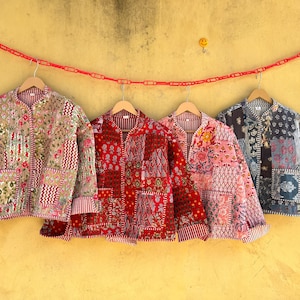 Puede incluir: Cuatro chaquetas acolchadas de varios colores y estampados cuelgan de perchas de madera contra una pared amarilla. Las chaquetas presentan diseños florales y geométricos en tonos rojos, rosas y azules. Cada chaqueta tiene un diseño de patchwork único.