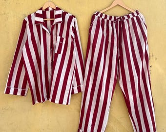 May include: A two-piece pajama set with a red and white striped pattern. The long-sleeved button-down shirt has a chest pocket. The matching pants have a drawstring waist. The set is hanging on a wooden hanger against a yellow wall.