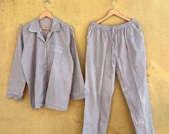Op de afbeelding: Een gestreepte pyjamaset, bestaande uit een overhemd met knopen en een broek, beide in een rood en blauw gestreept patroon op een lichte achtergrond. Het overhemd heeft een borstzak en de broek heeft een trekkoord. Witte rand.