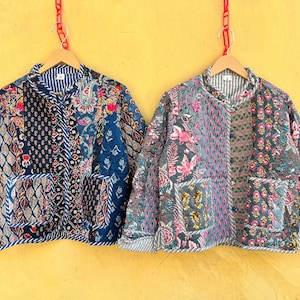 Puede incluir: Dos chaquetas acolchadas con estampados florales y geométricos cuelgan de una pared amarilla. Las chaquetas presentan una mezcla de tonos azules, rosas y grises, con diseños de patchwork y ribetes a rayas. Cada chaqueta tiene una percha de madera.