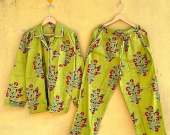 May include: A lime green pajama set with a floral pattern of red flowers and green leaves. The set includes a button-down shirt and matching pants with a drawstring waist. White trim accents the edges of the shirt and pants.