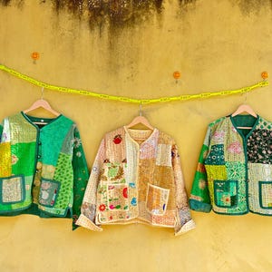 Op de afbeelding: Een set van drie keramische mokken met een gespikkelde, crèmekleurige glazuur. Elke mok heeft een handgeschilderd bloemmotief in blauw, groen en geel. De mokken hebben een eenvoudige, afgeronde vorm en een comfortabel handvat.